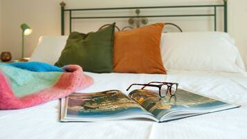 A bed with pillows, a blanket, and an open book with glasses on it.