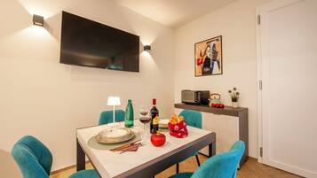 Un comedor con una mesa dispuesta para dos, un televisor de pantalla plana montado en la pared y una obra de arte enmarcada sobre la mesa.
