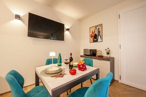Un comedor con una mesa dispuesta para dos, un televisor de pantalla plana montado en la pared y una obra de arte enmarcada sobre la mesa.