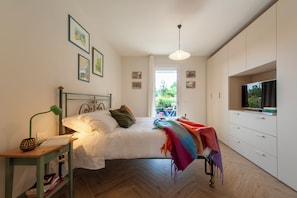A bedroom with a bed, a desk with a lamp, a television, and a window with a view of greenery. - Residence Case Nuove - Flo Apartments (Florence)