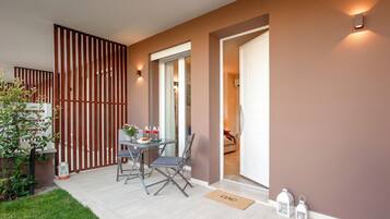 Un área de estar moderna al aire libre con una mesa, sillas, una planta en maceta y una puerta que da a un espacio interior.
