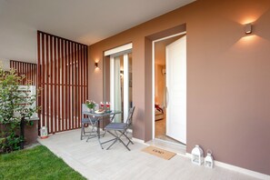 Un área de estar moderna al aire libre con una mesa, sillas, una planta en maceta y una puerta que da a un espacio interior.