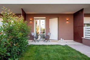 A modern outdoor patio with a dining table and chairs, a small garden area, and a sliding glass door leading to a balcony. - Residence Case Nuove - Flo Apartments (Florence)