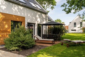 Une maison moderne dotée d’un patio comprenant une table, des chaises et deux transats.