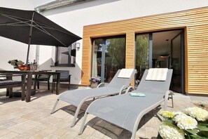 A patio with two lounge chairs, a table, and an umbrella. - Sandnelke, Domizil am Ostseewald (Zingst)
