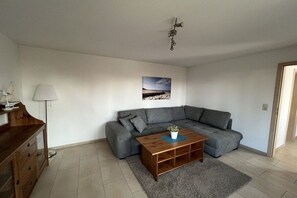 A living room with a grey sofa, a wooden coffee table, a lamp, and a picture on the wall. - Bungalow in Koserow with barbecue (Koserow)