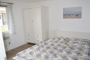 A bedroom with a bed, a wardrobe, a window with curtains, and a beach scene on the wall. - Bungalow in Koserow with barbecue (Koserow)