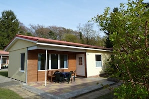 A small, single-story building with a red roof, a front porch with a table and chairs, and a door. - Bungalow in Koserow with barbecue (Koserow)