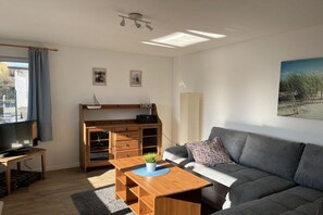 En moderne stue med sofa, sofabord, fjernsyn og et træskab.