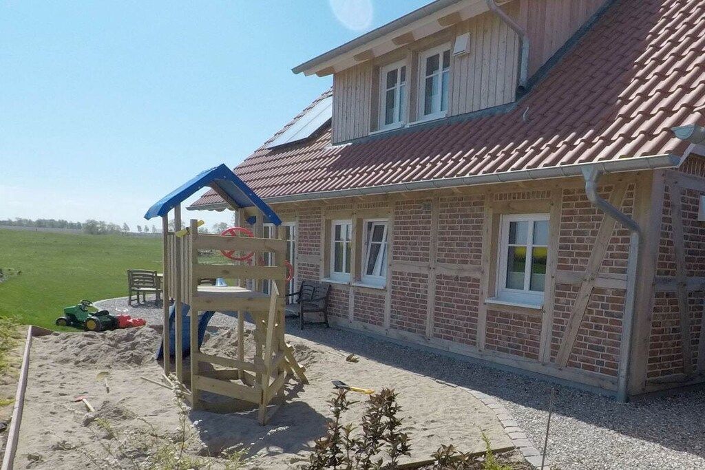 Une maison à deux étages avec un toit recouvert de tuiles rouges, une structure de jeu en bois et une terrasse dallée.