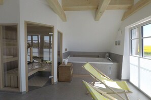 A modern interior with a large window, a bathtub, and a lounge chair.