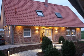 A brick house with a red tiled roof, two skylights, and a front porch with exterior lighting.