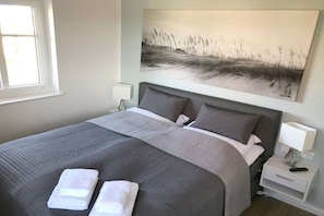 A hotel room with a large bed, two pillows, a nightstand with a lamp, and a painting on the wall.