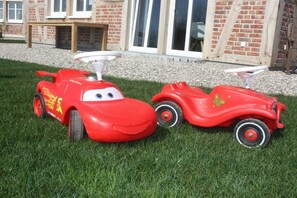 Two red toy cars on a grassy lawn with a brick building in the background.