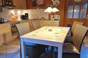 A kitchen with wooden cabinets, a dining table with chairs, a coffee maker, and a hanging light fixture. - Holiday home with 2 bedrooms (Börm\/nahe Kropp\/bei Schleswig)