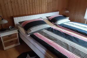 A double bed with striped bedding, a bedside table with a lamp, and a wooden headboard. - Holiday home with 2 bedrooms (Börm\/nahe Kropp\/bei Schleswig)