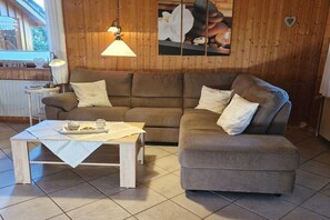A cozy living room with a brown sofa, a small table with a tray, and a hanging lamp. - Holiday home with 2 bedrooms (Börm\/nahe Kropp\/bei Schleswig)