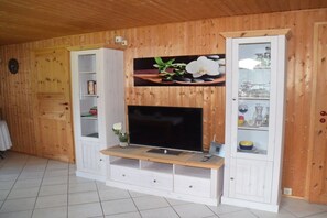 A wooden-paneled room with a television on a wooden stand, a white cabinet with glass doors, and a clock on the wall. - Holiday home with 2 bedrooms (Börm\/nahe Kropp\/bei Schleswig)