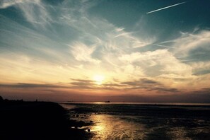 Ein Sonnenuntergang über einem Strand bei klar blauem Himmel und einem sichtbaren Kondensstreifen.