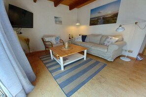Ein Wohnzimmer mit einem Holztisch, einer Couch, einem an der Wand montierten Fernseher und einer Lampe.