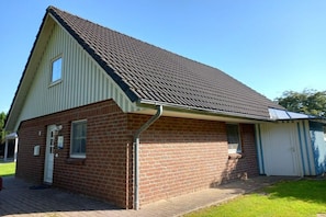 Ein eingeschossiges Backsteinhaus mit Satteldach, einer kleinen angebauten Garage und einem gepflasterten Einfahrt.