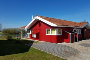 Un bâtiment rouge avec un toit en tuiles, une allée pavée et une petite pelouse avec un étang en arrière-plan.