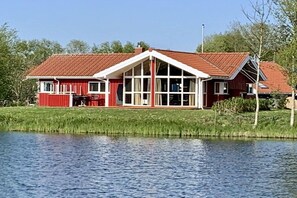 A red house with a white porch and a large window, situated by a body of water. - Holiday home with 1 bedroom (Otterndorf)