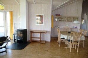 Ein Zimmer mit Kaminofen, einem Esstisch mit Stühlen, einer Bank und einem Bild an der Wand.