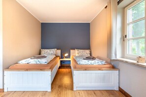A narrow room with two beds, a nightstand, and a window. - Holiday apartment with 2 bedrooms (Oevenum)