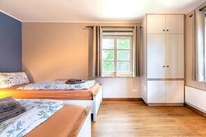 Une chambre avec deux lits, une fenêtre avec des rideaux, une armoire et un plancher en bois.