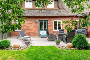 A brick house with a thatched roof, a patio with outdoor furniture, and a small garden. - Holiday apartment with 2 bedrooms (Oevenum)