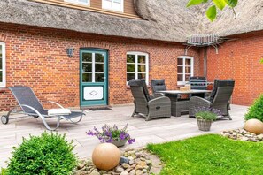 Une terrasse en briques avec une table et des chaises, un barbecue et une porte.