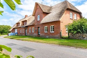 A traditional brick house with a thatched roof, a stone wall, and a paved driveway. - Holiday apartment with 2 bedrooms (Oevenum)