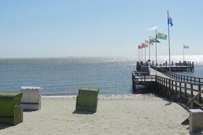 A beach with a wooden pier extending into the water, featuring flags and a clear sky. - Holiday apartment with 2 bedrooms (Oevenum)
