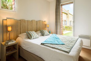 A neatly made bed with a striped pillow and a blue blanket, a bedside table with books, and a wall-mounted lamp. - Breton Alcove Stay for Six (Cancale)