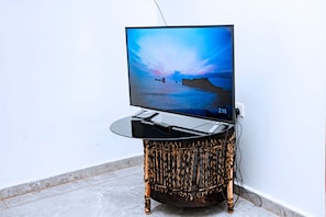 Un televisor de pantalla plana sobre una mesa redonda y trenzada, frente a una pared blanca.