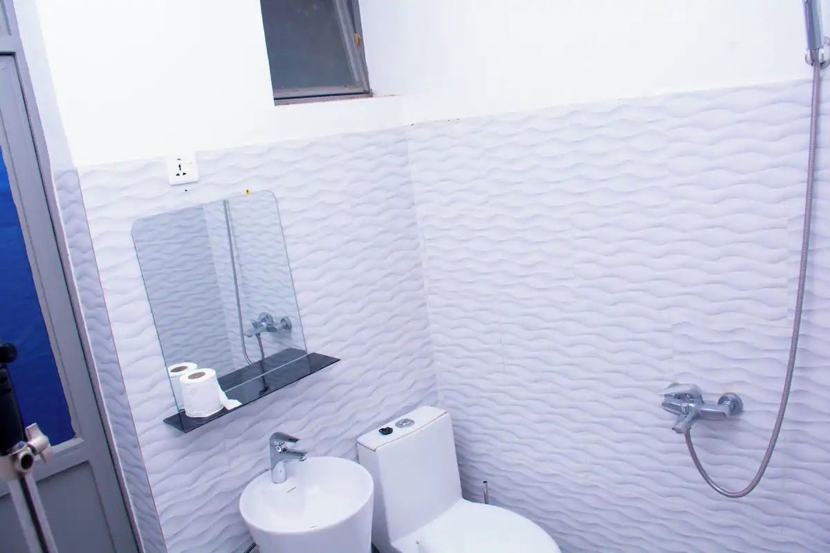 Ein Badezimmer mit weißer Wand, einem Waschbecken, einer Toilette, einem Spiegel und einer Dusche.