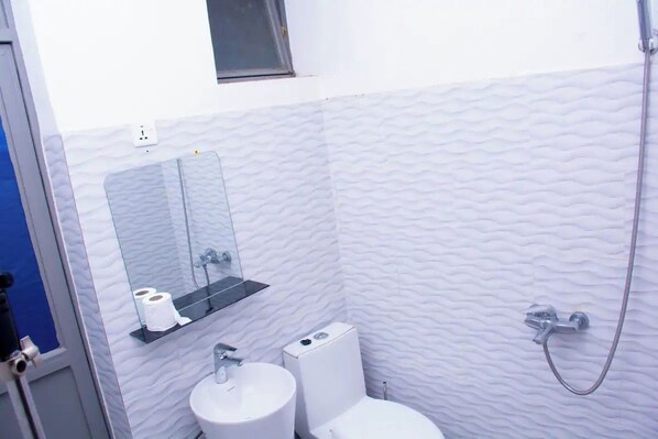 A bathroom with a white textured wall, a sink, a toilet, a mirror, and a shower.