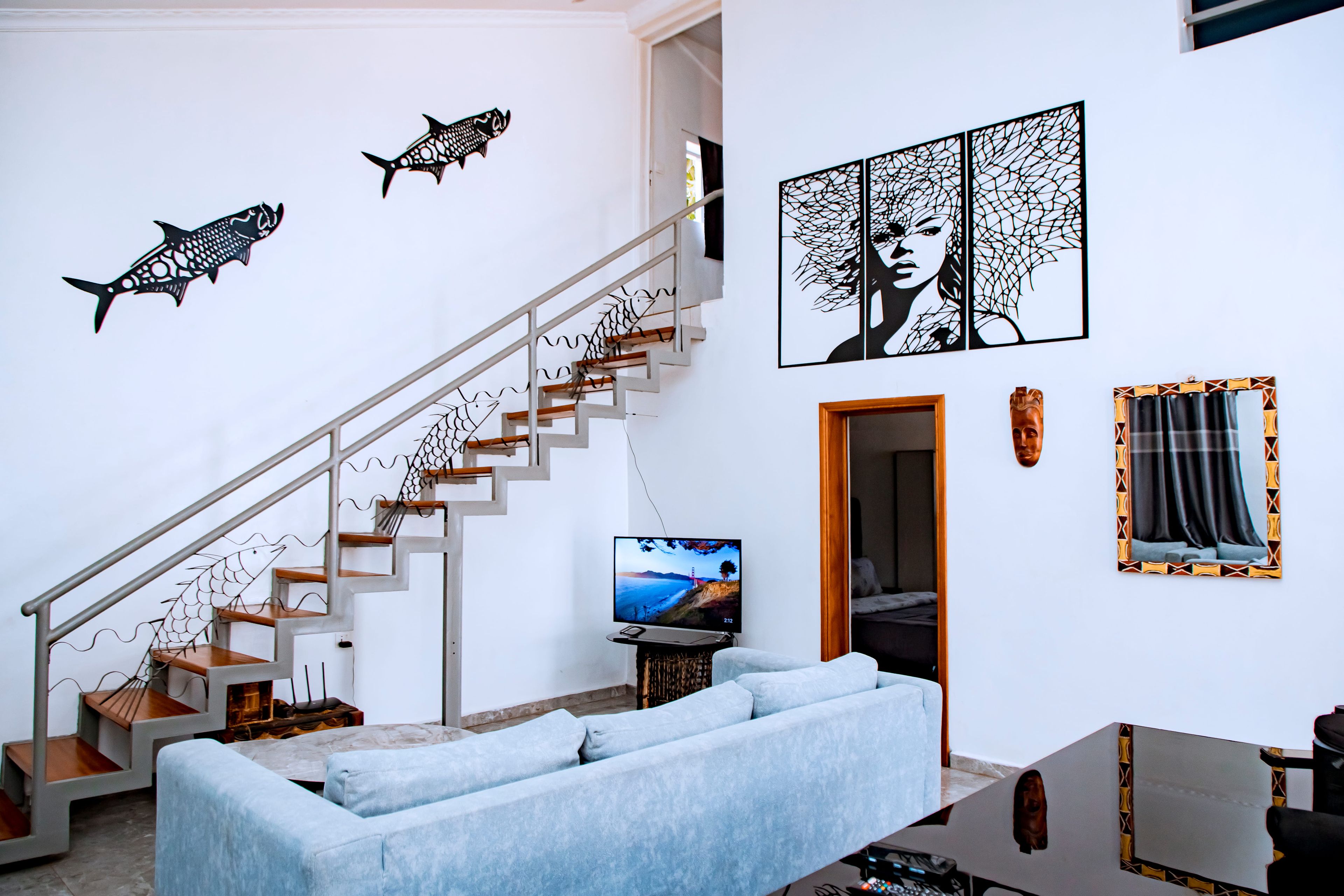 Una sala de estar moderna con una escalera, un televisor de pantalla plana, un sofá y decoración en la pared.