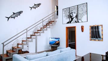 Una sala de estar moderna con una escalera, un televisor de pantalla plana, un sofá y decoración en la pared.