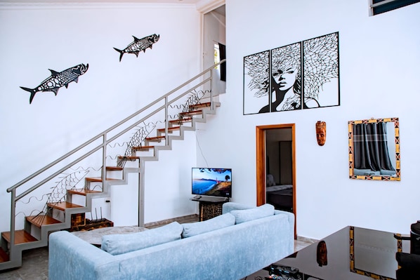 Una sala de estar moderna con una escalera, un televisor de pantalla plana, un sofá y decoración en la pared.