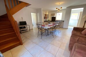 A spacious living area with a dining table set for four, a kitchen in the background, and a staircase leading to another level. - Provencal Family Getaway for Six (L'Isle-sur-la-Sorgue)