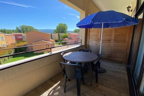 A balcony with a table and chairs, a blue umbrella, and a view of neighboring buildings. - Provencal Family Getaway for Six (L'Isle-sur-la-Sorgue)