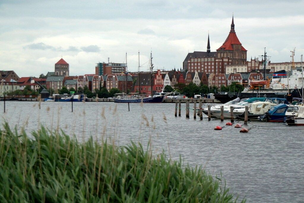 Ein Hafen mit vertäuten Booten, ein markantes Gebäude mit rotem Dach und eine Mischung aus traditioneller und moderner Architektur.