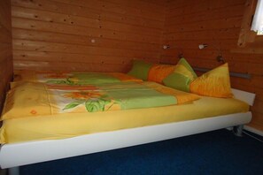 Ein Einzelbett mit blumigem Bettbezug und Kissen in einem Zimmer mit Holzwänden.