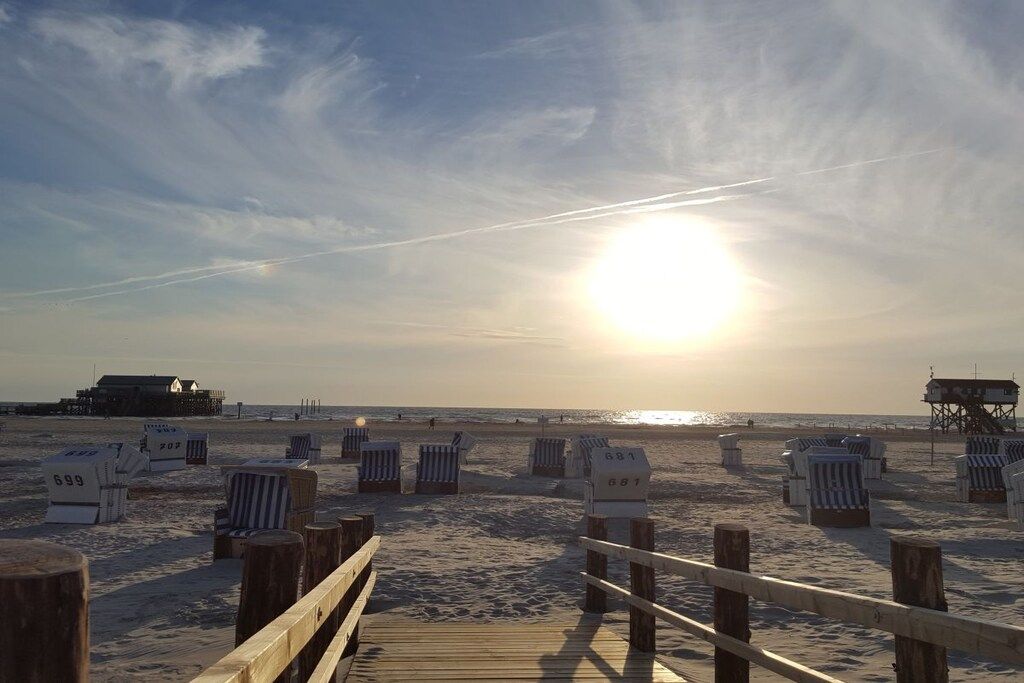 A beach with a wooden walkway leading to beach chairs marked with numbers.