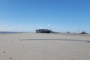 A beach with a pier structure and a lighthouse in the distance. - Hein Godenwind - Julia (Sankt Peter-Ording)