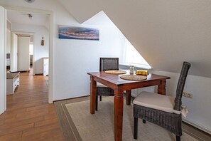 A dining area with a wooden table and wicker chairs, a painting on the wall, and a view of the interior. - Hein Godenwind - Julia (Sankt Peter-Ording)
