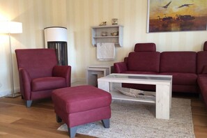 A living room with a red sofa, a matching ottoman, a white coffee table, a floor lamp, and a painting on the wall. - Boddenhus "Crane Rest" (Born am Darss)