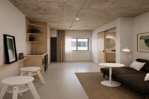 Ein modernes Wohnzimmer mit einer Couch, zwei weißen Tischen, einem Teppich und einer Küchenzeile mit Spüle und Schränken.